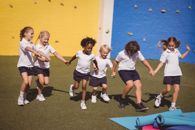 Children running hand in hand in a schoolyard, showcasing friendship, teamwork, and active play. Ideal for educational materials, advertisements promoting outdoor activities, and content emphasizing childhood joy and diversity.