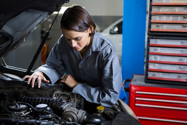 Female mechanic working on car engine in auto shop. Useful for articles and advertisements related to automotive services, women in male-dominated professions, car repair workshops, and vocational training. Could also be used in blogs or promotional materials to highlight gender diversity in the automotive industry.