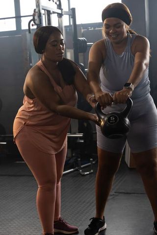 African american coach and trainee doing kettlebell workout together in gym studio wearing sneakers