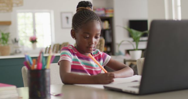 Image of thoughtful african american girl writing during online class on laptop at home, copy space. Education, learning, technology and domestic life.