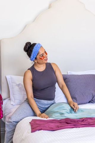 Young woman relaxing on bed with under-eye gel patches and headband for at-home spa