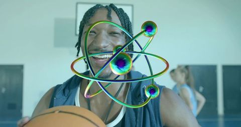Smiling basketball player holding ball with iridescent atom overlay in gym court