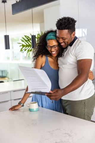 African american couple reading document while embracing in modern sunlit kitchen