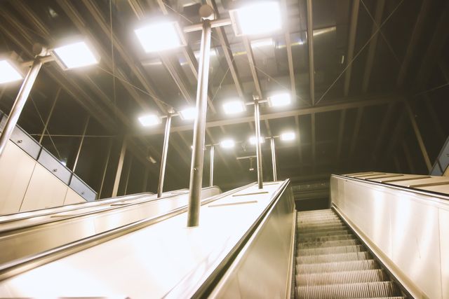 The image features modern escalators ascending with bright overhead lights creating a futuristic atmosphere, ideal for content on urban infrastructure, modern transportation systems, or architectural design highlights.