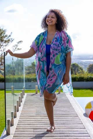 Smiling african american woman walking barefoot on pool deck in colorful swim kaftan