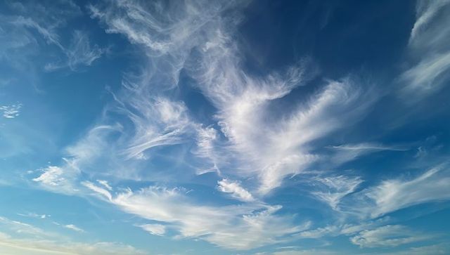 Feather-like cirrus cloud plumes filling expansive blue sky