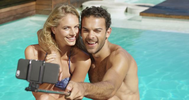 Happy couple taking selfie sitting by the pool