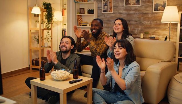 Friends clapping and cheering during cozy living room movie night with popcorn