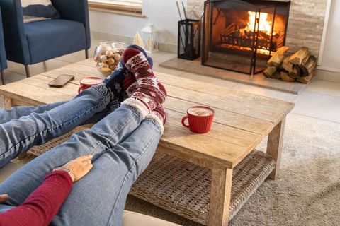 Couple relaxing by fireplace wearing festive socks and denim jeans with red mugs