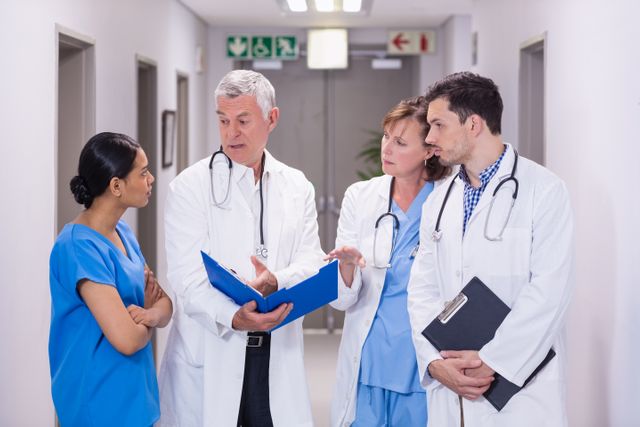 Nurse and doctors discussing over clipboard in hospital corridor