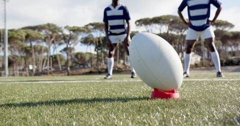 Rugby ball on tee with players in position on field, team strategy concept