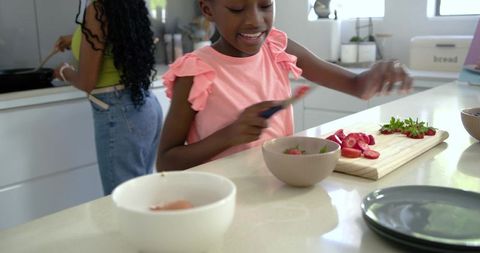 African mother and daughter slicing strawberries on bright modern kitchen island