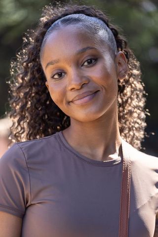 Serene african young woman smiling with curly ponytail wearing mauve top outdoors