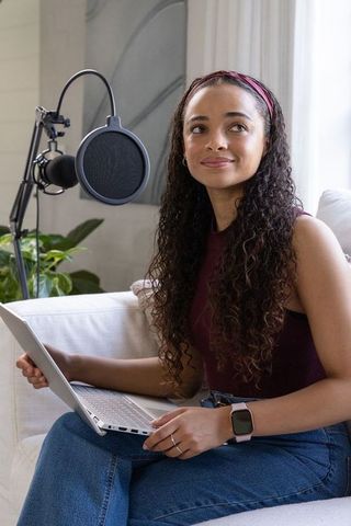 African american woman recording podcast with laptop and microphone in minimalist studio