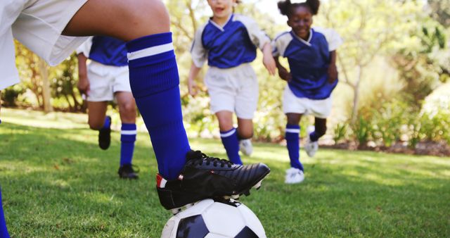 Children engaged in a soccer game, with a player wearing a blue uniform stepping on the ball surrounded by teammates in the background. Perfect for promoting youth sports, team activities, and fitness-related content.