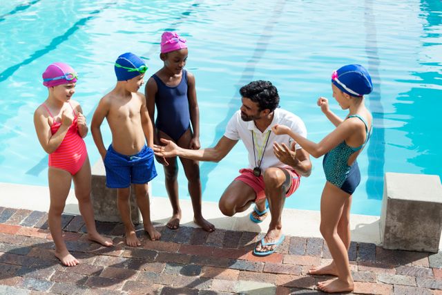High angle view of male trainer assisting children at poolside