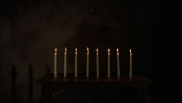 Glowing nine white twisted taper candles casting long shadows on dark carved wooden table