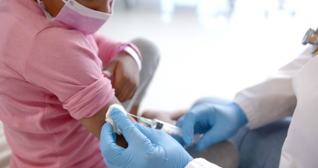 Depicts a healthcare professional administering a vaccination to a young child who is wearing a mask. The image can be used for medical or health-related articles about vaccinations, pediatric healthcare, immunization campaigns, or promoting the importance of protective measures like wearing masks. Suitable for use by clinics, hospitals, educational materials, and public health campaigns.