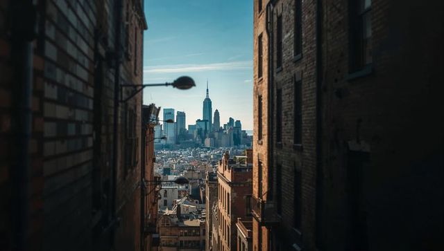 Narrow brick alley framing distant skyline with spire and streetlamp silhouette