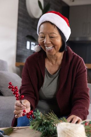 Senior Woman Crafting Holiday Wreath in Santa Hat at Home
