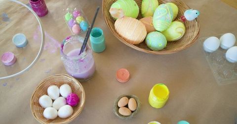 Easter egg crafting workspace showing pastel hand-painted eggs, paint jars, woven baskets