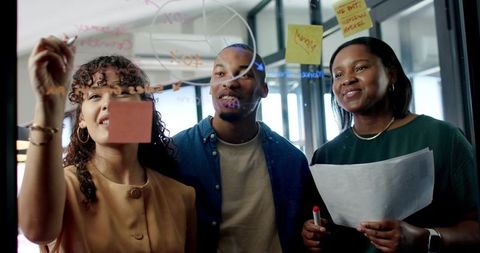 African american coworkers brainstorming at glass board in modern open-plan office