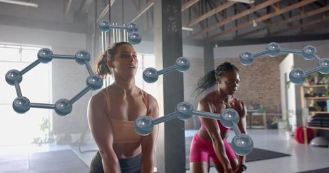 Two women swinging kettlebells in industrial loft gym with molecular overlay graphics
