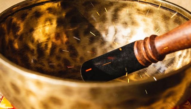 Hand-hammered tibetan singing bowl resonating with wooden mallet and golden sparks