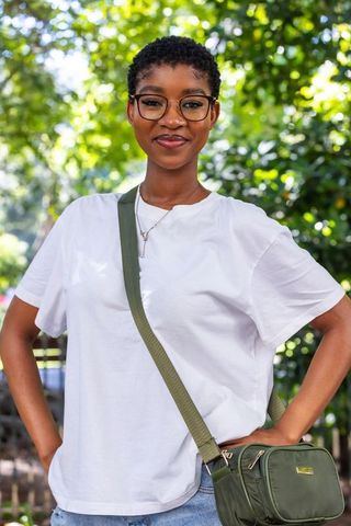 Confident african american woman wearing white tee, glasses and olive crossbody bag in park