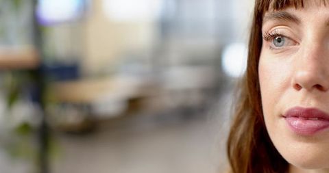 Calm professional woman looking right in modern office headshot with soft bokeh background
