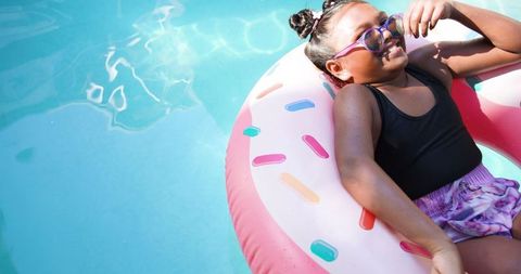 Child relaxing on donut float in pool on sunny day