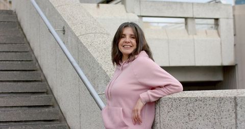 Smiling woman leaning on concrete railing wearing pink hoodie on urban stairs