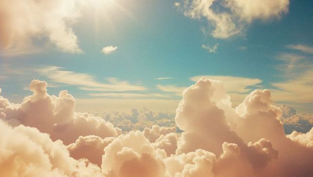 Sunlight Streaming Through Fluffy White Clouds in Clear Blue Sky