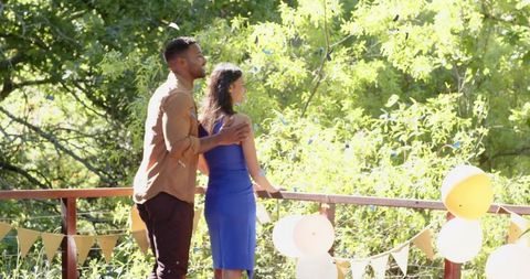 Romantic couple embracing on sunny terrace with balloons and bunting, greenery view