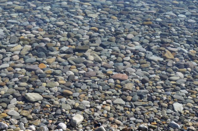 Tranquil scene of smooth stones under clear, calm water. Perfect for themes related to nature, body of water, tranquility, and natural landscapes. Ideal for use in environmental awareness campaigns, meditation or relaxation materials, and natural resource management presentations.