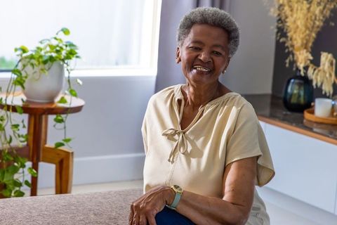 Senior woman smiling while sitting in sunlit living room with plants and neutral decor
