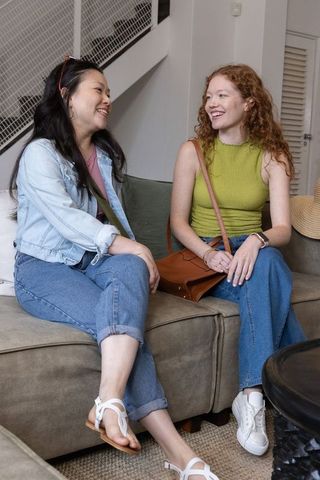 Friends chatting and smiling on couch wearing denim and green top, casual home hangout