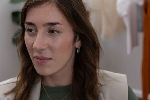 Thoughtful woman gazing left in neutral dressing area wearing green crewneck and beige vest