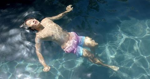 Teenage Boy Peacefully Floating in Clear Pool Water, Sunlit Day