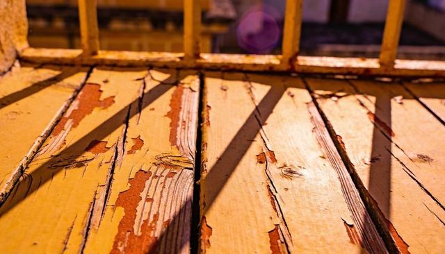 Sunlit peeling yellow floorboards with railing shadows and rustic wood grain texture