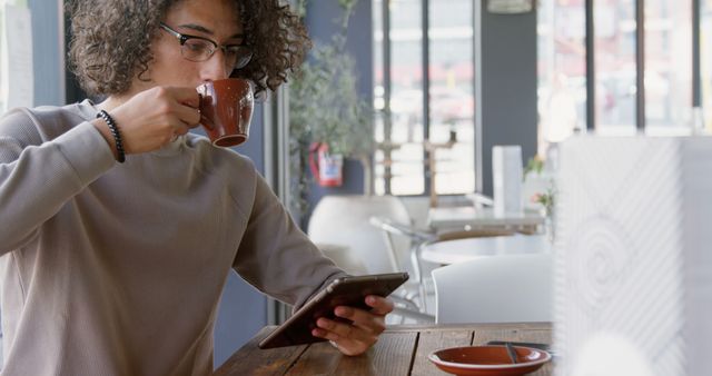 Young Woman Drinking Coffee while Reading on Tablet in Cafe - Download Free Stock Images Pikwizard.com