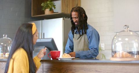 Smiling african american barista serving croissant to customer at café counter