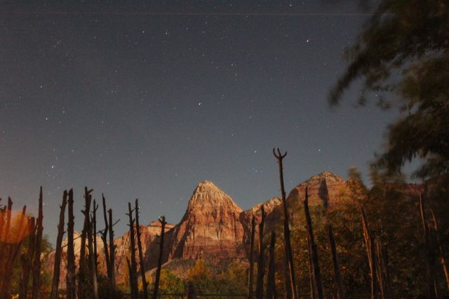 Night sky littered with stars above mountainous terrain with wooden fence in the foreground. Ideal for nature and travel publications, serenity visuals, and wilderness adventure promotions.