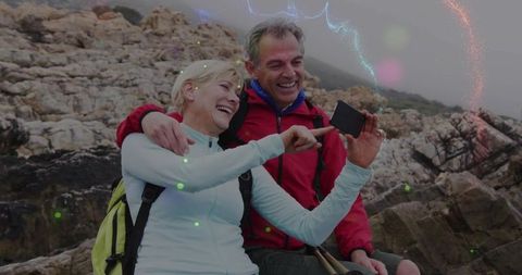 Senior Couple Hiking on Rocky Coast Holding Smartphone and Poles