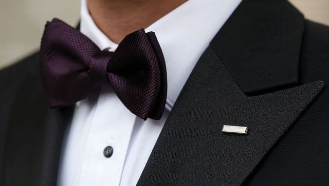 Dapper man wearing dark purple bow tie and black tuxedo with silver lapel pin