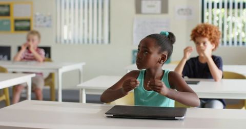 Young student gesturing attentively in modern classroom with closed laptop on desk
