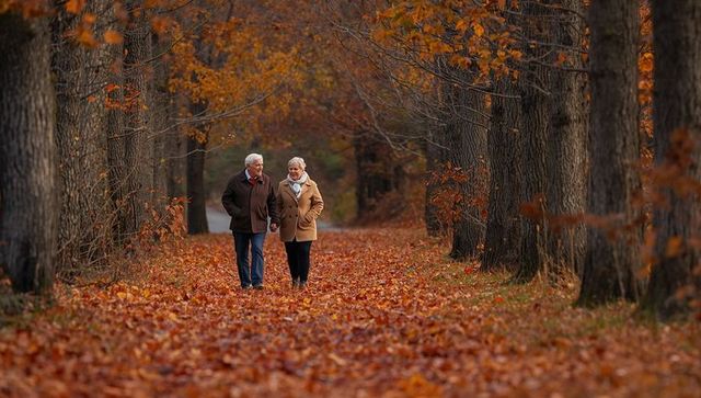 Senior couple walking hand-in-hand along tree-lined path covered in autumn leaves
