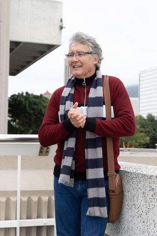 Mature man standing on city terrace wearing striped scarf, glasses and brown messenger bag