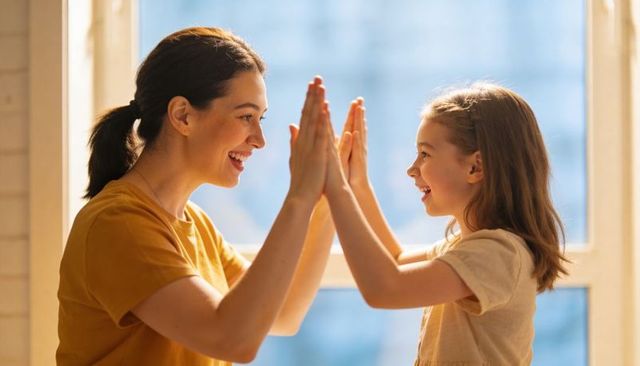 Mother and daughter sharing joyful high-five by sunlit window
