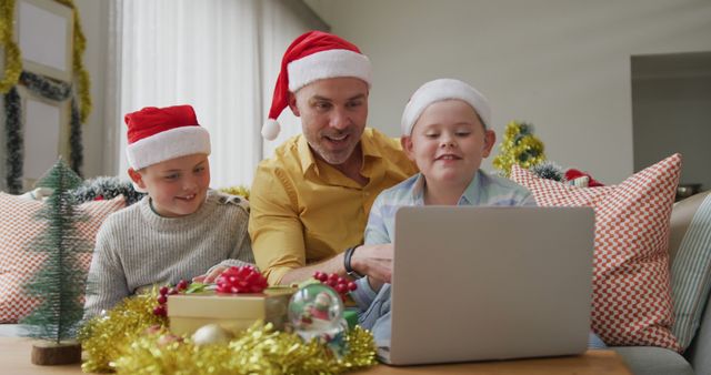 Father and children wearing Santa hats gathered around laptop in living room decorated for Christmas. Great for holiday-themed advertisements, family bonding, and promoting festive activities and products.